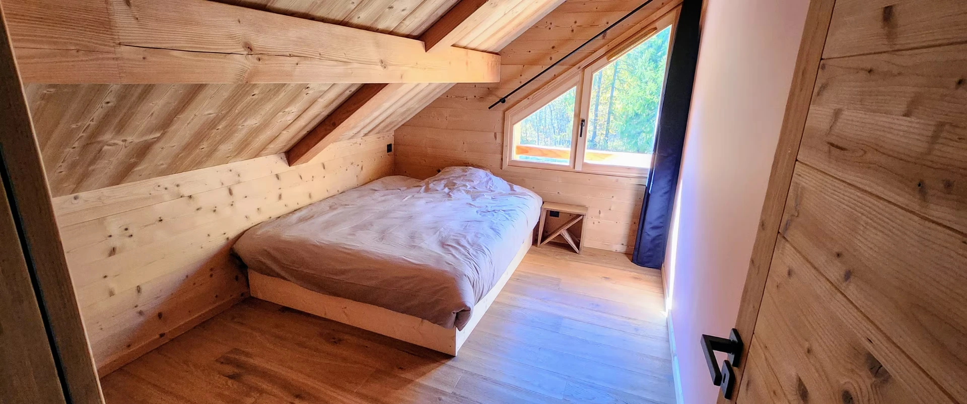 Camera matrimoniale in mansarda con finestra sul bosco e soffitto spiovente