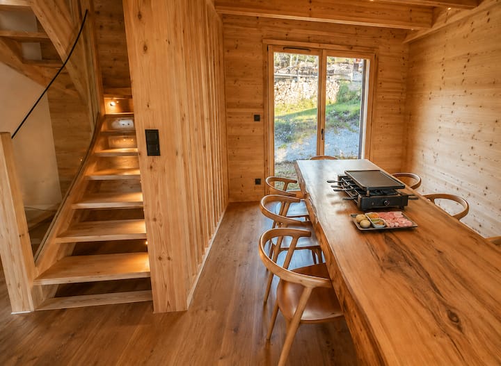 Tavolo comune in legno con raclette, sedie e scala interna della baita